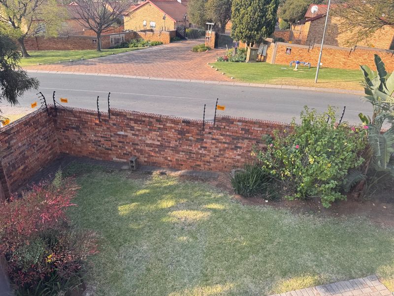 An elevated view of a private rear garden featuring a brick boundary wall with electric fencing, overlooking a quiet residential street.