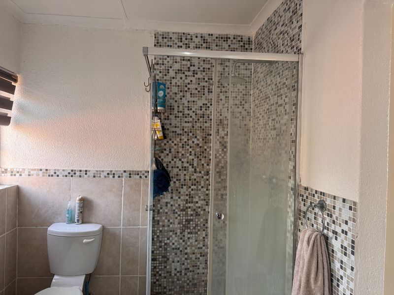 A functional bathroom featuring a shower enclosure with mosaic tiling, a standard toilet, and neutral ceramic wall tiles.