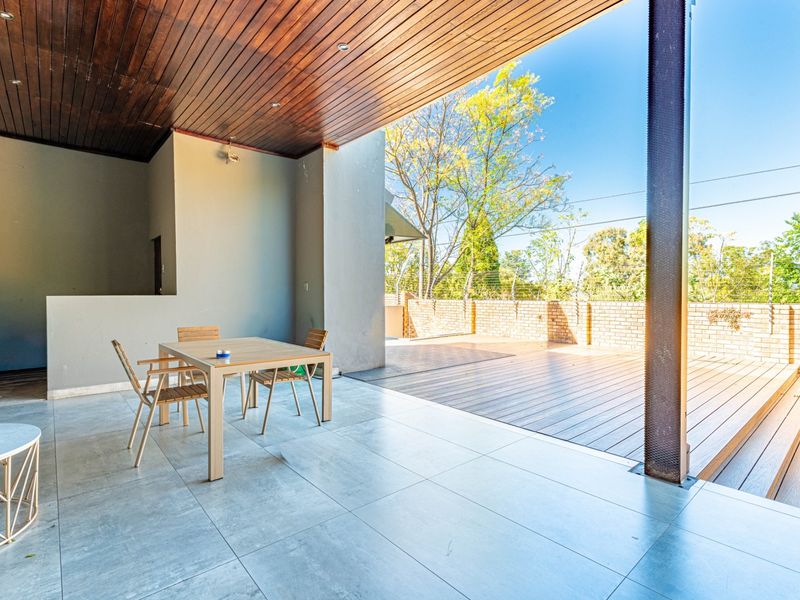 Spacious covered patio featuring a timber ceiling with recessed lighting, tiled flooring, and an adjoining timber deck overlooking the garden.