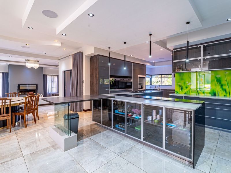 Modern open-plan kitchen and dining area featuring high-gloss cabinetry, a central island with glass accents, tiled flooring, and contemporary recessed ceiling lighting.
