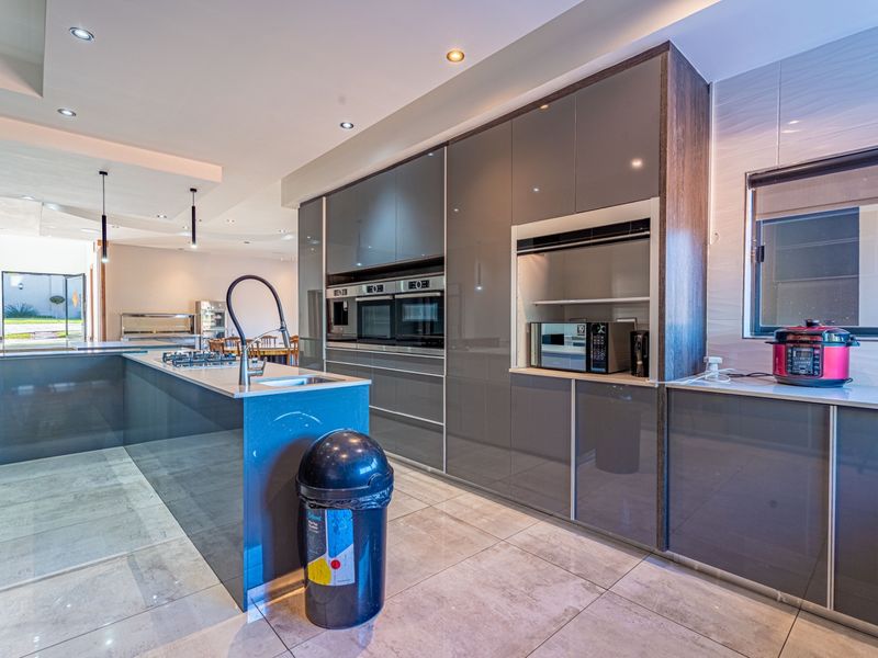 Modern kitchen featuring high-gloss cabinetry, stone countertops, a central island with a gas hob, and integrated built-in appliances.