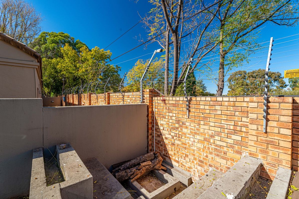 A rear exterior area featuring a brick boundary wall secured with electric fencing and concrete structural elements.
