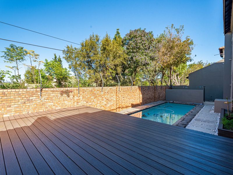 Outdoor pool area featuring a composite deck, brick boundary wall with electric fencing, and a paved walkway alongside the swimming pool.