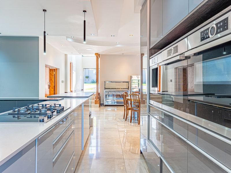 Modern kitchen featuring high-gloss cabinetry, stone countertops, integrated gas cooktop, and built-in ovens, flowing into an open-plan living area with polished tile flooring.