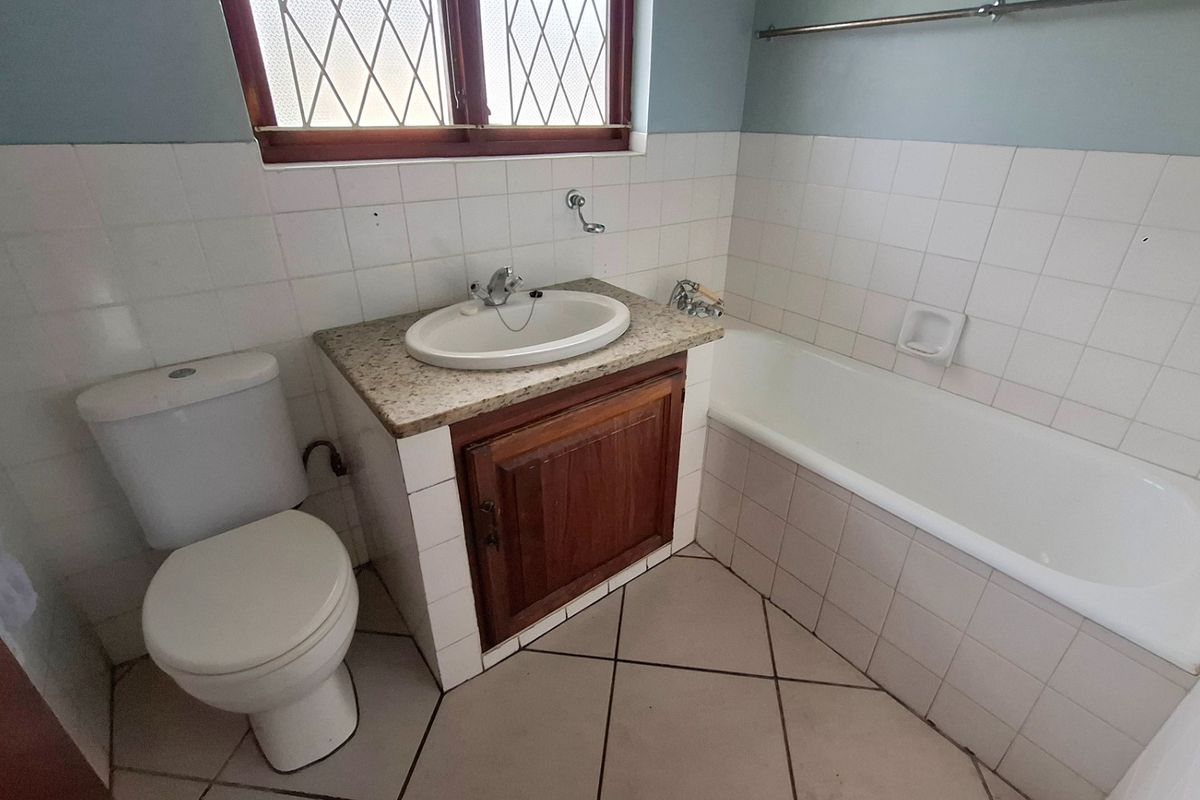 A dated bathroom featuring a vanity with granite countertop, a standard toilet, and a bathtub with tiled surround and flooring.