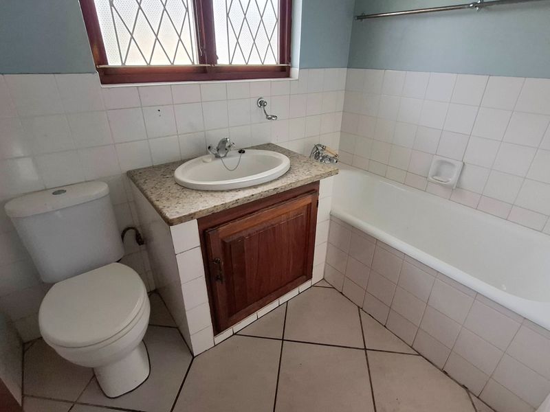 A dated bathroom featuring a vanity with granite countertop, a standard toilet, and a bathtub with tiled surround and flooring.