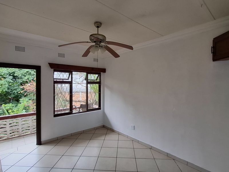 An empty living room featuring tiled floors, a ceiling fan, and direct access to an outdoor balcony area.