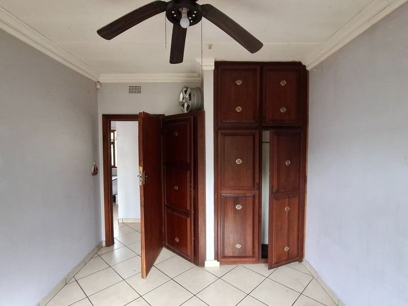 A bedroom featuring tiled flooring, a ceiling fan, and built-in wooden cupboards, offering a functional space ready for personalization.