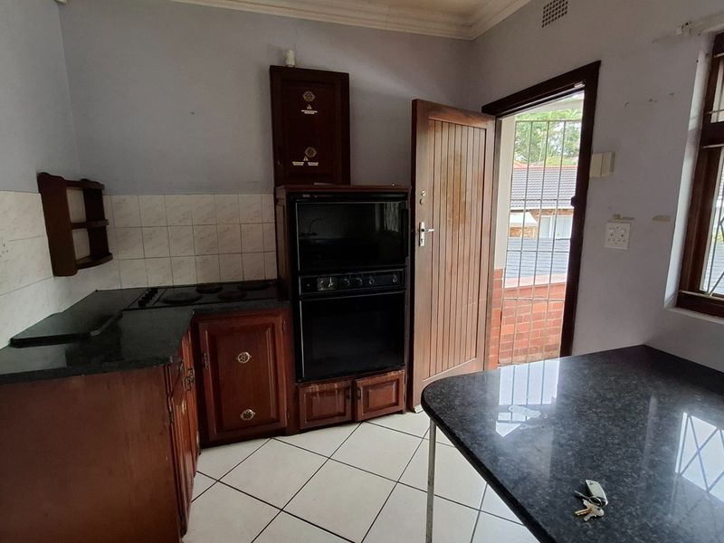 A functional kitchen featuring dark wood cabinetry, granite countertops, built-in oven and hob, tiled flooring, and direct access to an exterior area.
