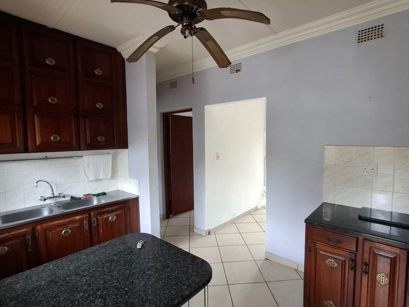 A functional kitchen featuring dark wooden cabinetry, granite countertops, a double sink, and tiled flooring, offering a classic layout ready for modernization.