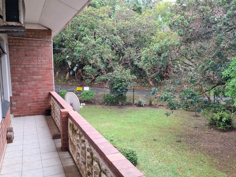 A covered balcony featuring tiled flooring, brick walls, and a decorative concrete screen, overlooking a private garden area.
