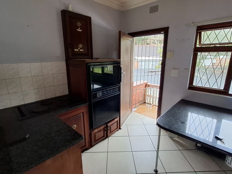 A functional kitchen featuring built-in oven, electric hob, tiled backsplash, and wooden cabinetry, with direct access to an outdoor balcony area.