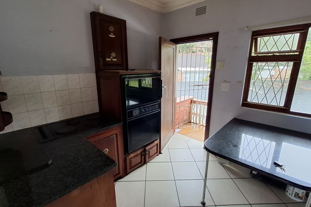A functional kitchen featuring built-in oven, electric hob, tiled backsplash, and wooden cabinetry, with direct access to an outdoor balcony area.
