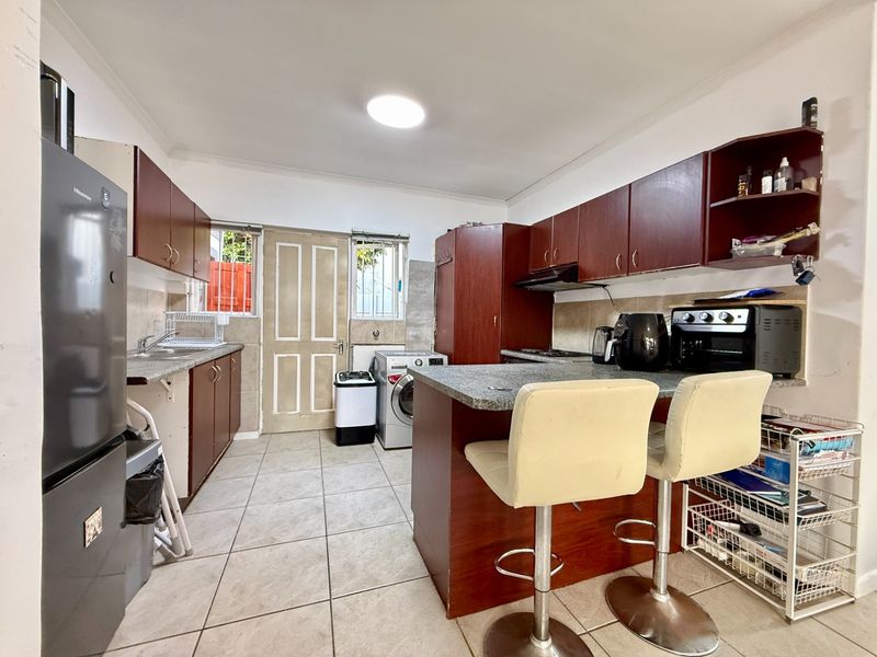 Functional kitchen featuring dark wood cabinetry, granite countertops, tiled flooring, and an integrated breakfast nook area with direct exterior access.