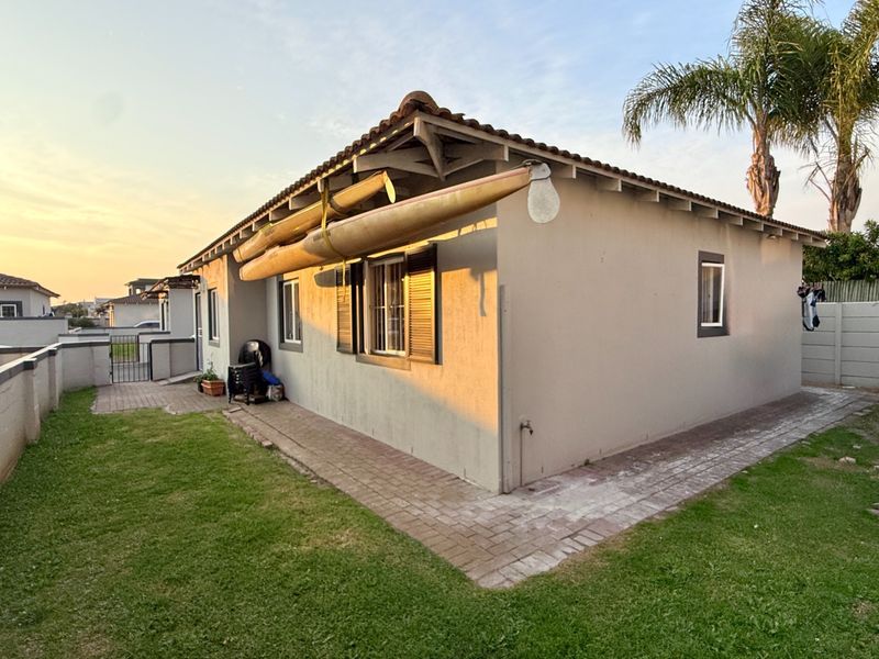 Rear view of the house featuring a tiled roof, paved perimeter walkway, and established garden area.