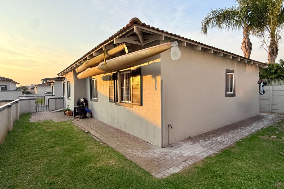 Rear view of the house featuring a tiled roof, paved perimeter walkway, and established garden area.