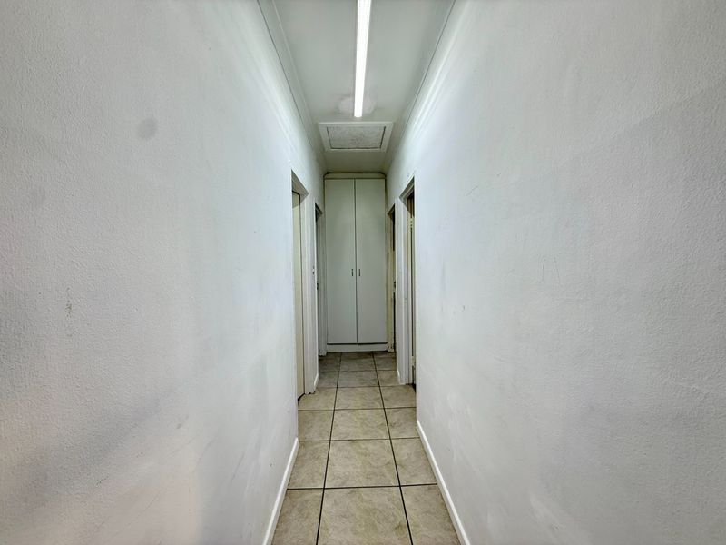 A functional hallway featuring tiled flooring, a built-in storage cupboard, and a ceiling access hatch, requiring minor cosmetic updates to the wall finishes.