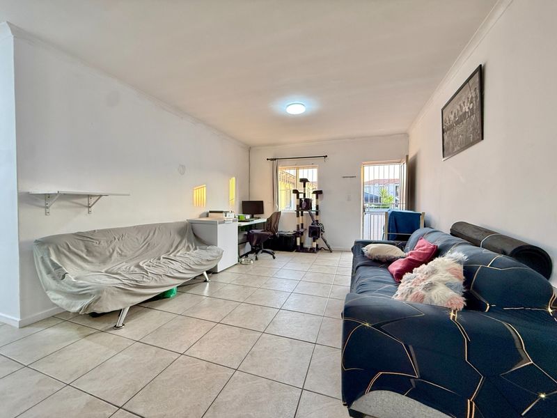A functional living room featuring tiled flooring, coving, and direct access to the exterior via a security gate.
