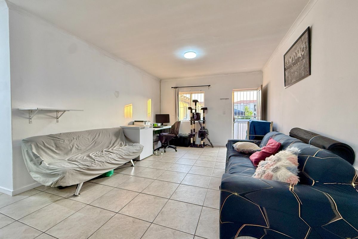 A functional living room featuring tiled flooring, coving, and direct access to the exterior via a security gate.