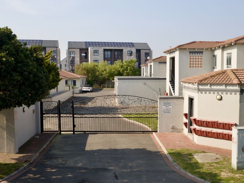 A secure gated entrance to a residential complex featuring paved driveway access, perimeter walls, and tiled roof structures.
