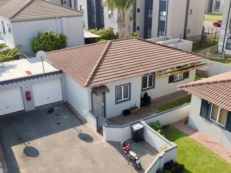 Aerial view of a residential property featuring a tiled roof, double garage, paved driveway, and enclosed garden area within a complex.