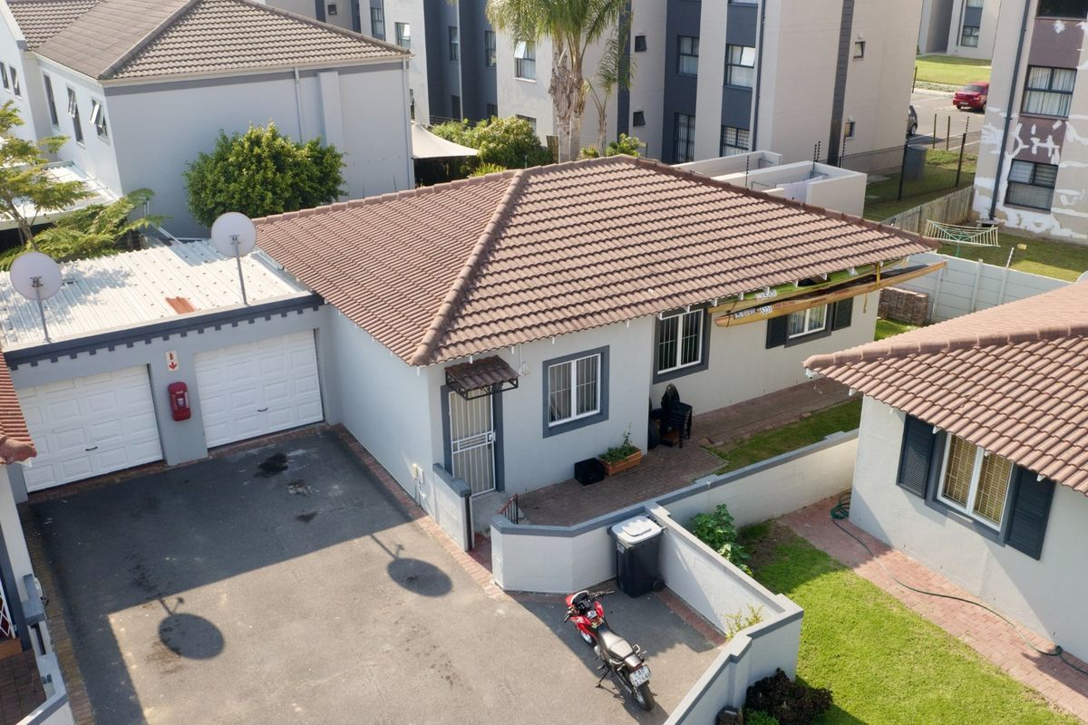 Aerial view of a residential property featuring a tiled roof, double garage, paved driveway, and enclosed garden area within a complex.