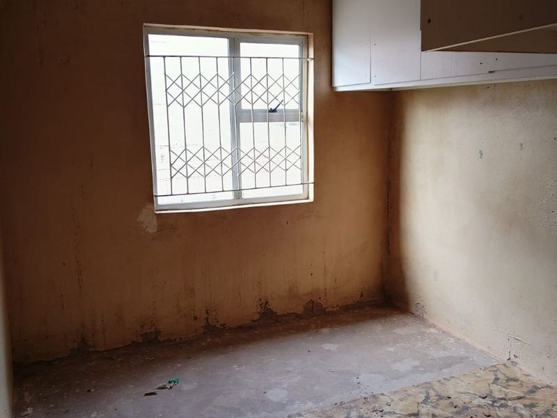 An empty bedroom featuring built-in cupboards, a security gate on the window, and ceiling tiles, requiring significant renovation and flooring replacement.