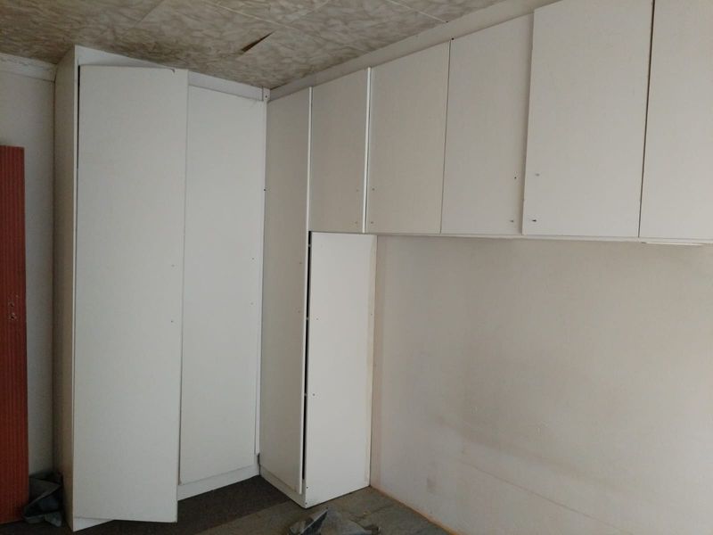 An empty bedroom featuring white built-in cupboards, requiring ceiling repairs and flooring installation to complete the space.