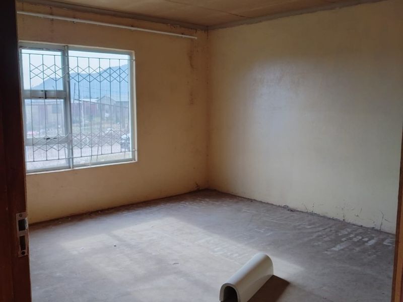 An empty bedroom featuring a security gate on the window, unfinished concrete flooring, and plain wall finishes, requiring cosmetic updates and flooring installation.