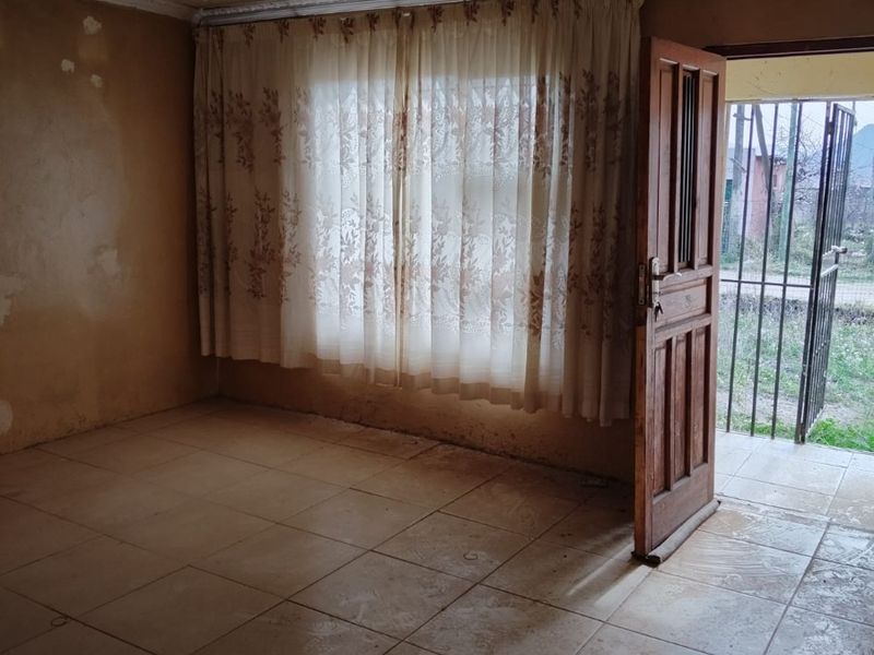 An empty living room featuring tiled flooring, decorative ceiling molding, and a timber entrance door leading to an exterior security gate.