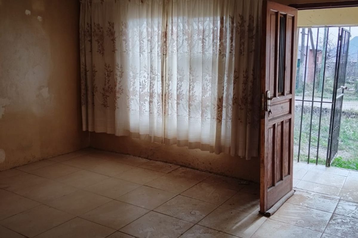 An empty living room featuring tiled flooring, decorative ceiling molding, and a timber entrance door leading to an exterior security gate.