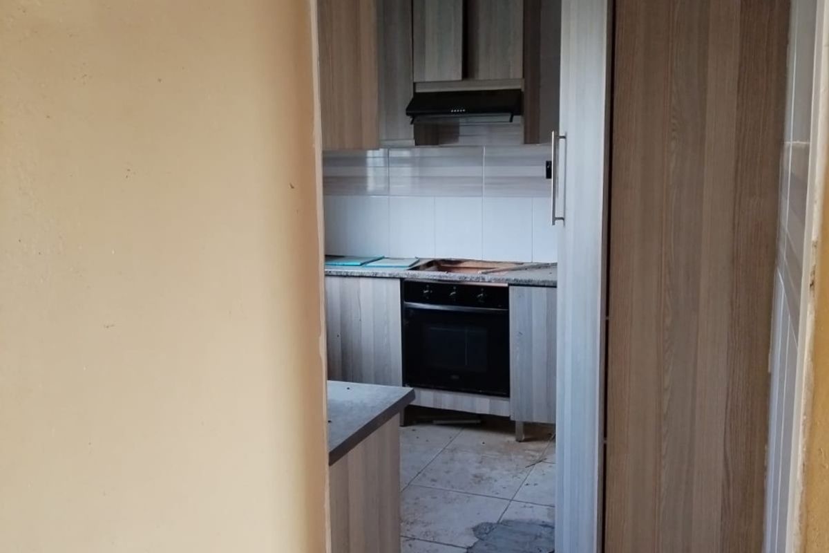 A small, dated kitchen featuring built-in cabinetry, an oven, and an extractor fan, currently in need of significant renovation and cleaning.