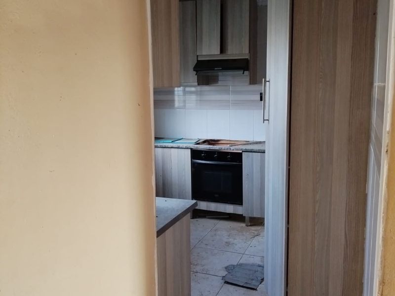 A small, dated kitchen featuring built-in cabinetry, an oven, and an extractor fan, currently in need of significant renovation and cleaning.