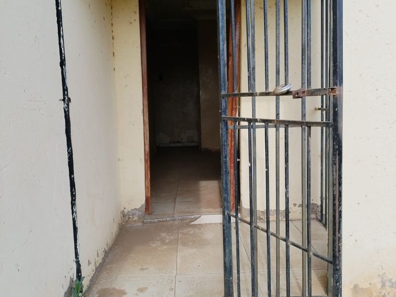 Entrance area featuring a metal security gate and tiled threshold, showing significant wear and requiring maintenance to the wall finishes and flooring.