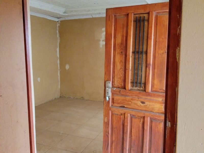An empty bedroom featuring tiled flooring, a coved ceiling, and a wooden door with an integrated security grille, requiring cosmetic updates and wall repairs.