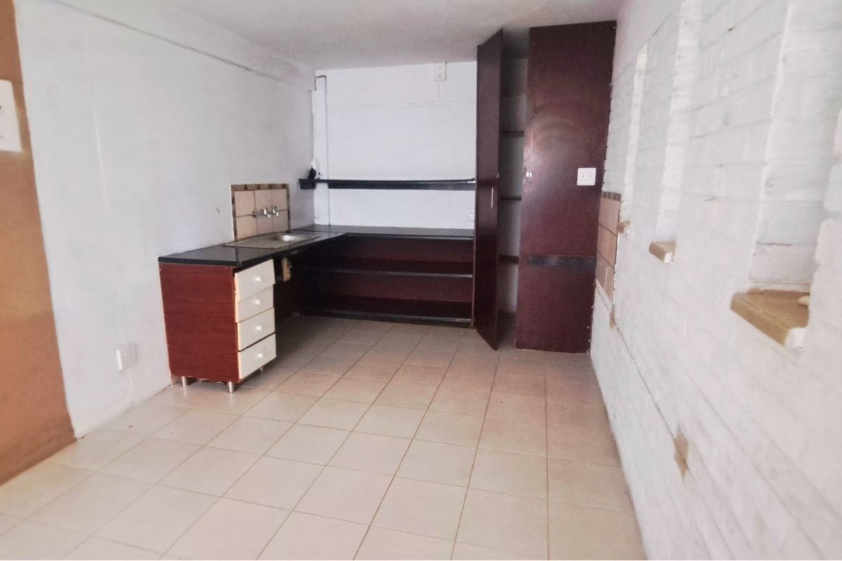 A compact, empty kitchen area featuring basic built-in cabinetry, a sink, and tiled flooring, ready for renovation or modernization.