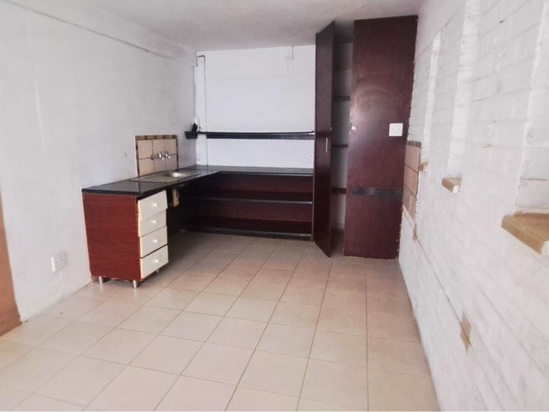 A compact, empty kitchen area featuring basic built-in cabinetry, a sink, and tiled flooring, ready for renovation or modernization.