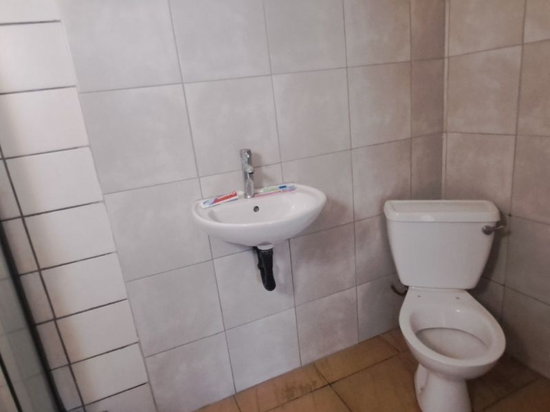 A functional bathroom featuring a wall-mounted basin, a standard toilet, and a shower enclosure with tiled walls and flooring.