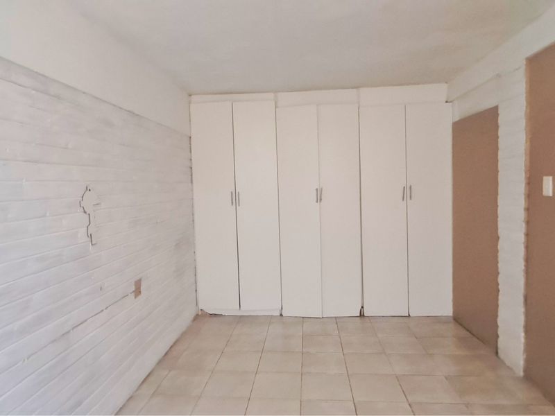 An empty bedroom featuring tiled flooring, built-in cupboards, and painted brick walls, offering a blank canvas for renovation or interior design updates.