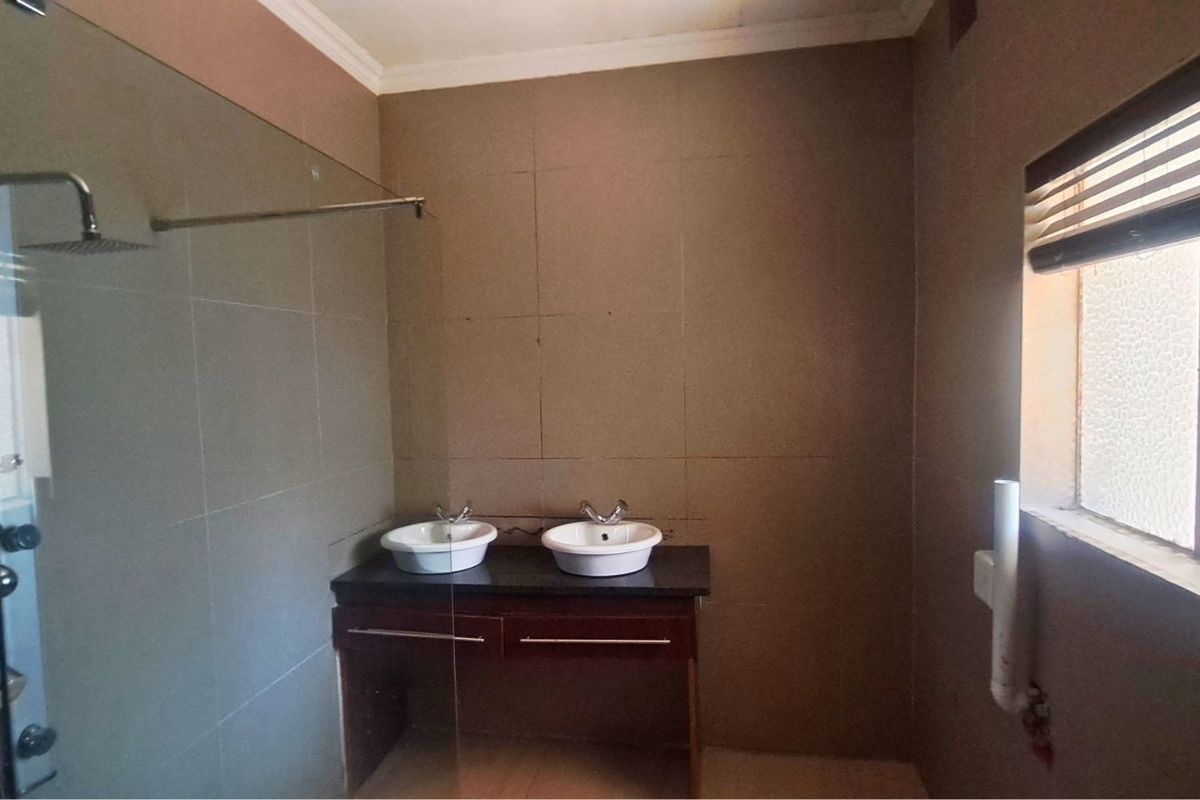 A bathroom featuring a double vanity with vessel sinks, a glass-enclosed shower panel, and tiled walls.