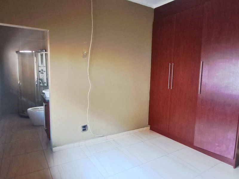 A bedroom featuring built-in cupboards, tiled flooring, and an en-suite bathroom visible through the doorway.