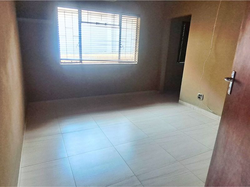 An empty bedroom featuring tiled flooring and a window with security bars, requiring minor cosmetic updates and electrical finishing.