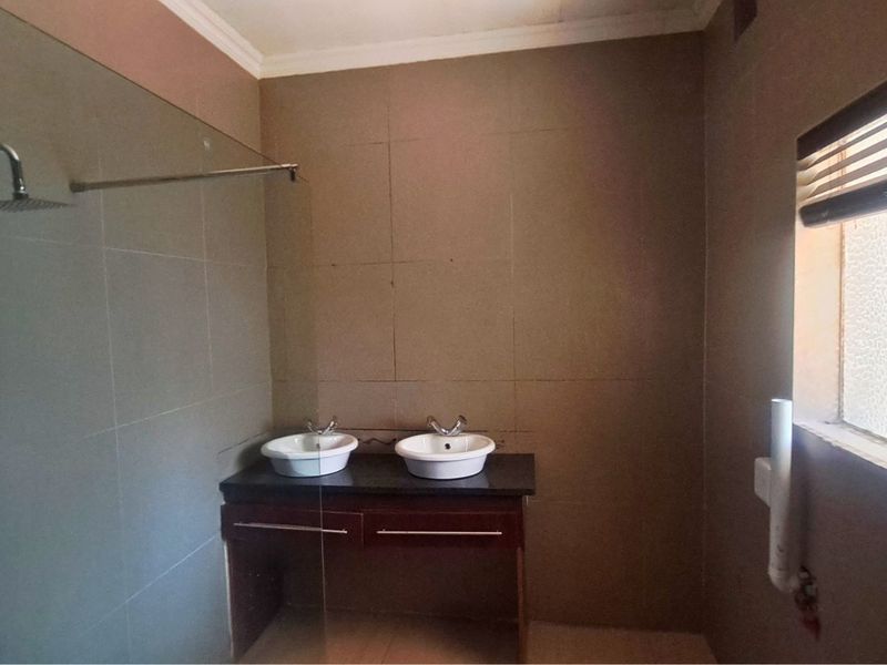 A bathroom featuring a double vanity with vessel sinks, a glass-enclosed shower panel, and tiled walls.
