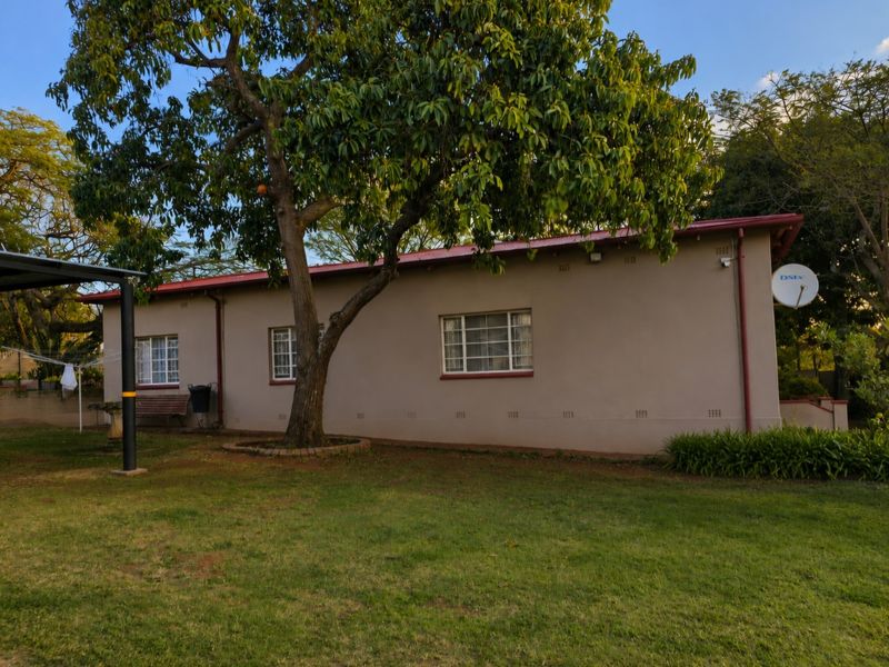 A view of the rear exterior of the house featuring a metal roof, security bars on windows, and a well-maintained garden area.