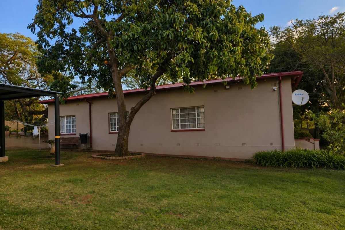 A view of the rear exterior of the house featuring a metal roof, security bars on windows, and a well-maintained garden area.