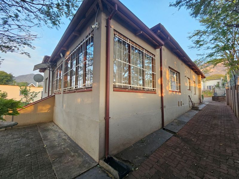 Rear exterior view of the house featuring paved walkways, security bars on windows, and external drainage systems.