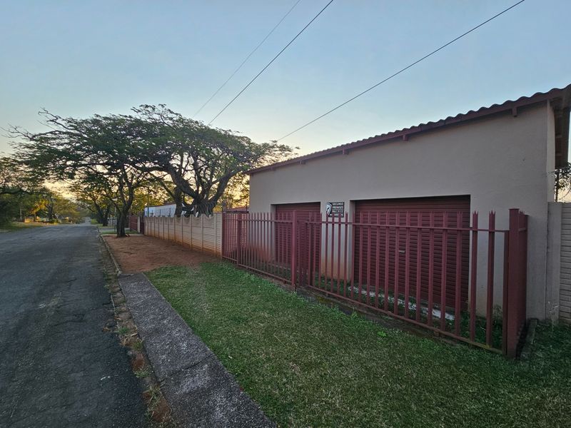 Street view of the property featuring a double garage with roller shutter doors and secure steel palisade fencing along the perimeter.