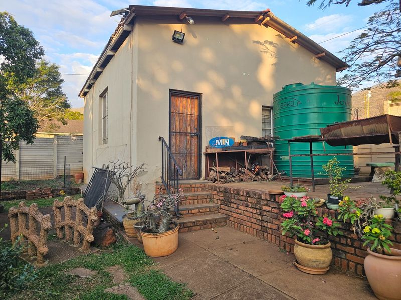 Rear exterior view of the property featuring a brick retaining wall, concrete steps, security gate, and a large water tank.