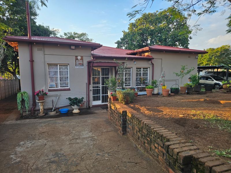 Rear view of the house featuring a corrugated metal roof, security-gated entrance, and a brick retaining wall bordering the garden area.