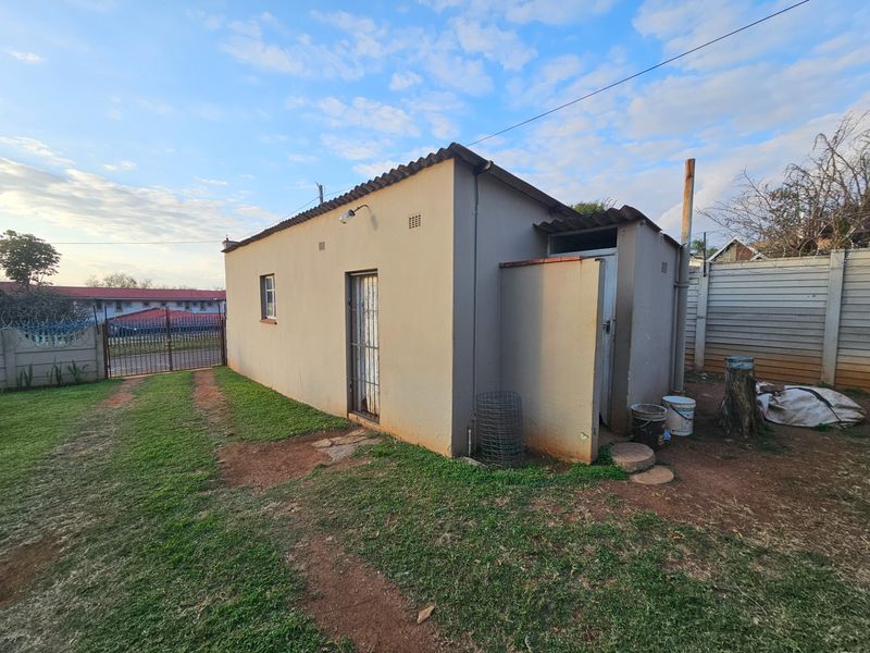 Rear view of the property showing the exterior structure, corrugated roofing, and surrounding yard area with precast boundary walling.